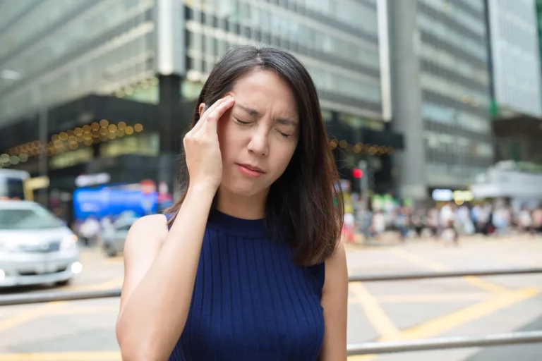 Lady walks in a city with her hand holding her head, obviously in pain.